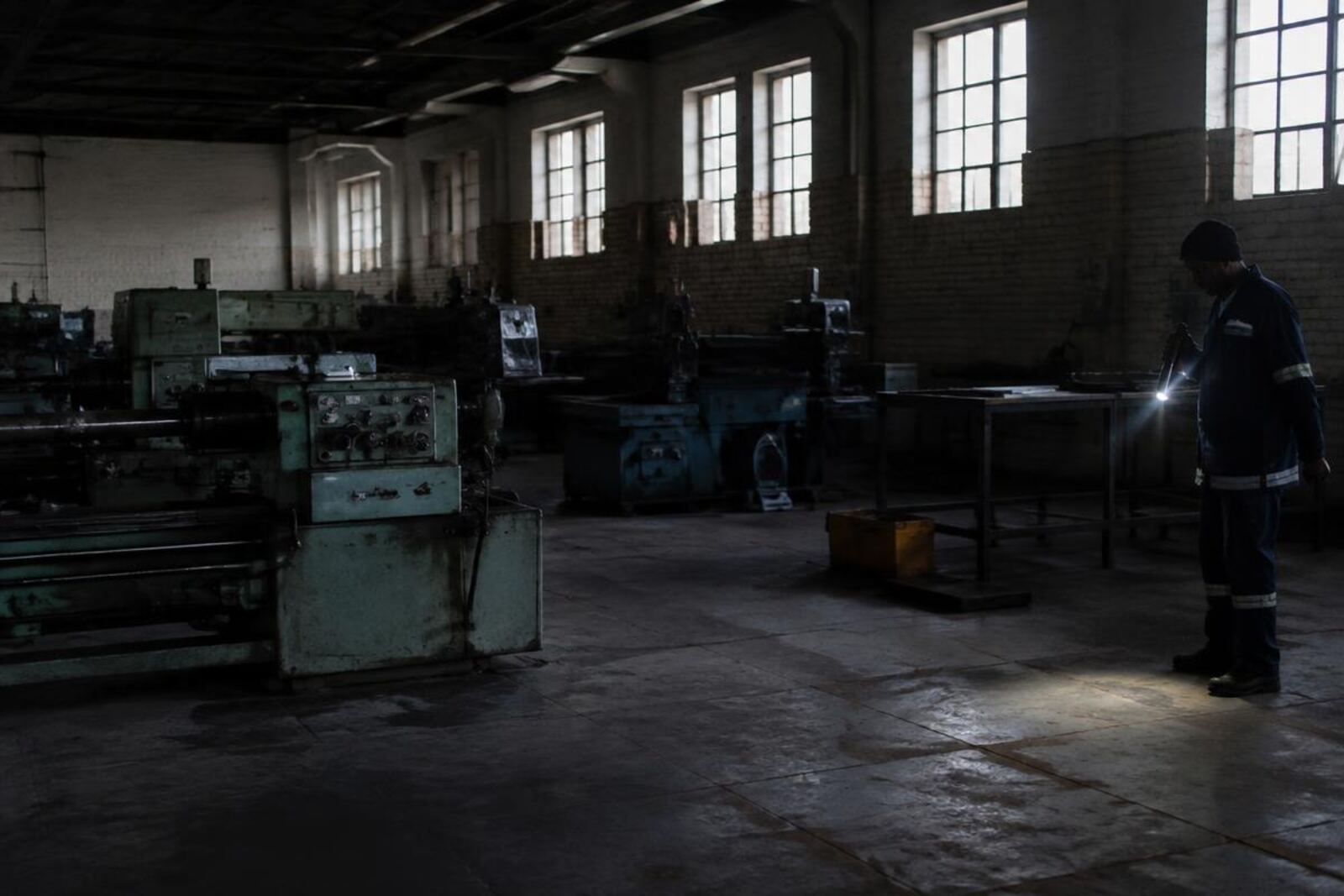 Worker with a torch inspecting an idle factory floor
